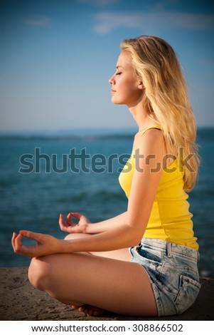 Beautiful blond woman meditating on a beach at sunrise in early summer - morning meditation on a sea coast