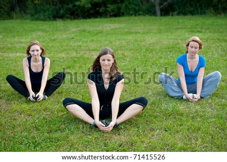 Group meditation - three cute girls meditates outdoor on a green grass field in park