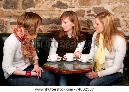 Three beautiful young students drinking  coffee and having a debate in coffee shop
