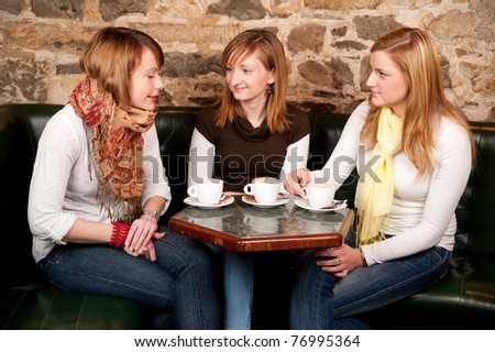 Three beautiful young students waiting drinking  coffee and having a debate in coffee shop