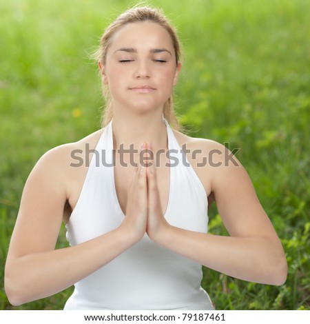 Meditation in nature - Cute young girl meditates outdoor on a green grass field in park