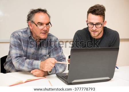 Young man teaching elderly man of usage of computer. Inter generational transfer of computer skills.