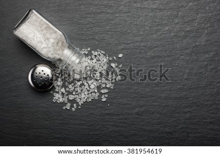 sprinkled salt shakers of white salt on the stone black background, top view
