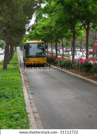 Spanish yellow bus in a narrow lane with trees and green hedges alongside