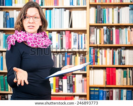 Woman with writing pad gesturing in front of bookshelves