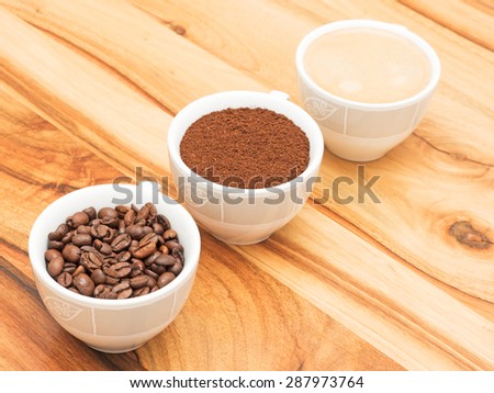 Three cups with coffee, coffee beans and ground coffee on wooden table