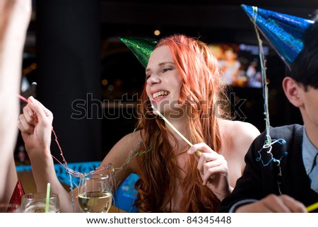 A young woman with long red hair amidst a celebration, wearing a party hat and covered with streamers.