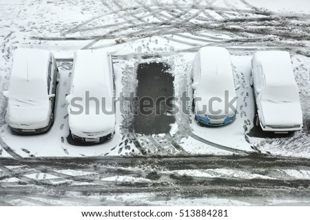Ground parking cars after snowfall, view from above. Automobiles covered with snow, the traces of wheels and legs.