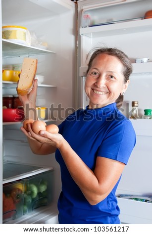 Beauty mature woman taking in fridge of   kitchen interior
