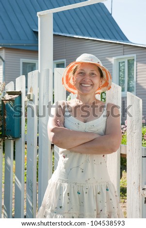 beautiful older woman with a hat stands at the gate of a country house
