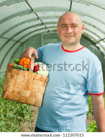 man with basket of harvested vegetables in greenhouse