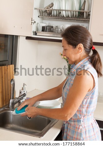 Positive housewife washing plates with sponge in domestic kitchen