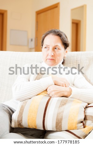 moody senior woman sitting on sofa at home
