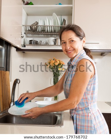 Positive housewife washing plates with sponge in domestic kitche