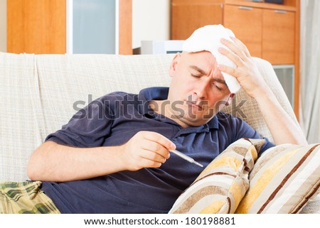 Illness  man with thermometer stupes  towel to her head at home