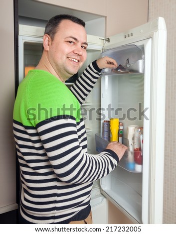 Handsome guy near opened refrigerator in kitchen at home