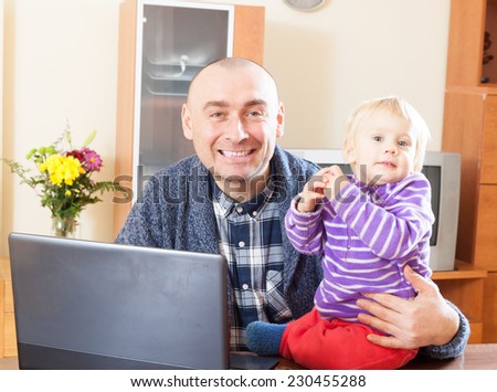 Adult dad sitting at  laptop with  young daughter on his lap