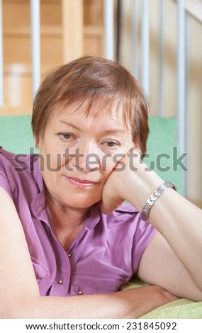 Stressed female pensioner laying on her elbows and thinking indoor