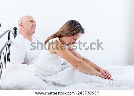 offended woman sitting on   bed next to   frustrated man.