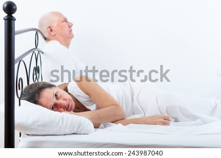 Sad mature woman  turned away from   elderly man sitting on   bed