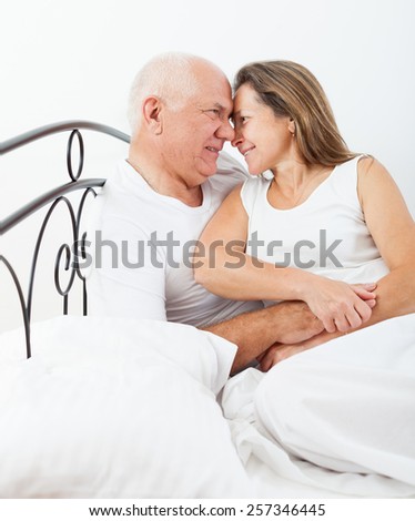 Senior  man and   woman resting on   bed in   embrace.