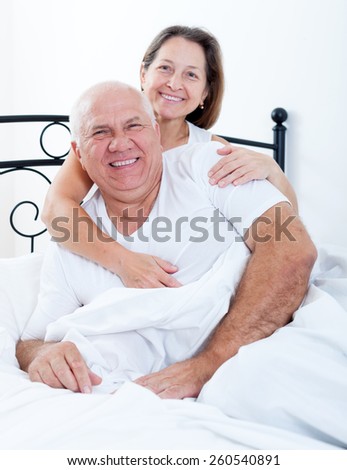 Senior  man and   woman resting on   bed in   embrace.