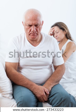 Sad senior man  turned away from   mature woman sitting on   bed
