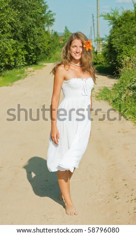 Summer girl in white dress goes for a walk on rural road