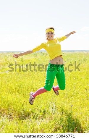 Jumping fit girl in coloured sporting suit in a summer park