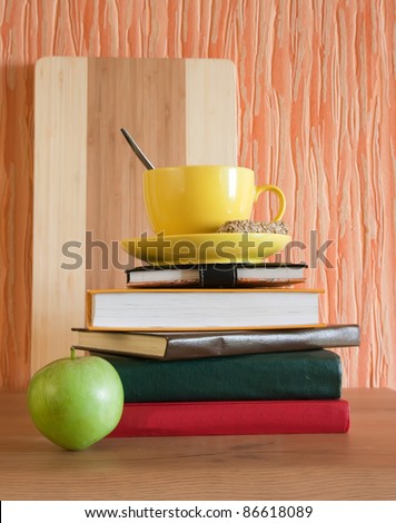 Yellow cup of tea with sweet cakes on heap of books