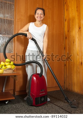 Cheerful expression worn by a well uniformed housekeeper. She is vacuuming the entry foyer into  home.