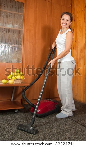 Cheerful expression worn by a well uniformed housekeeper. She is vacuuming the entry foyer into  home.