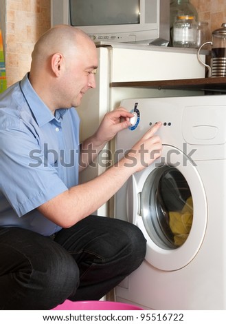 Young man loading the washing machine in kitchen