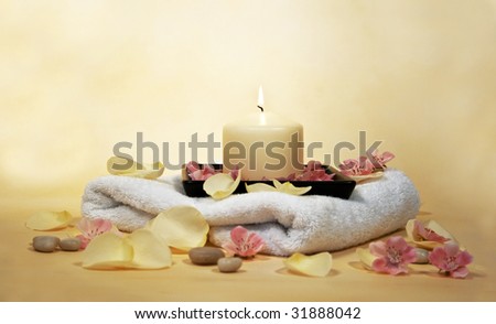 white towel with yellow candle and rose leaves and little stones