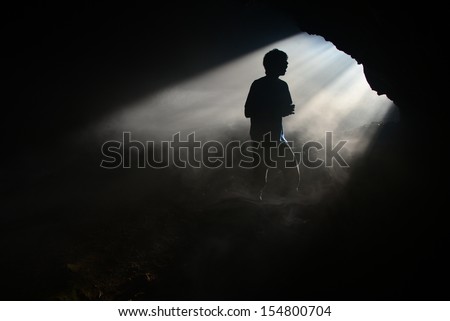 A silhouette of a person at a mine entrance with sunlight passing through.