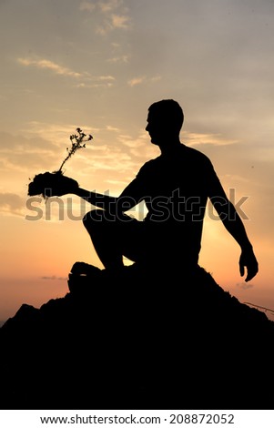 A human silhouette at sunset holding a plant with a piece of earth.