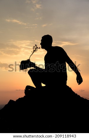 A human silhouette at sunset holding a plant with a piece of earth.
