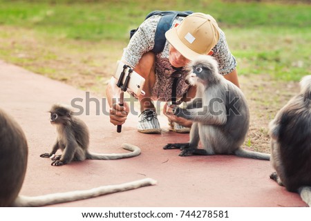 Travel selfie with funny monkeys. Young man takes a picture of wild animals. Spectacled langurs leave their isolated rocky forest to visit people to get food in Prachuap Khiri Khan, Thailand