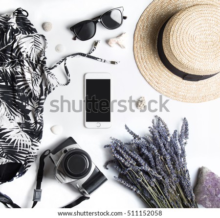 Stylized feminine flatlay with swimming suit, sunglasses, camera, hat, bunch of lavender, crystal stone, sea shells and smart phone mock up isolated on white top view. Woman accessories from above.