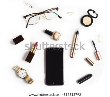 Flat lay, top view feminine table desk isolated on white.  Workspace with cosmetics, phone, glasses, lipstick, nail lacquer, watches, mascara and eyeshadow in gold. Golden and black tones.