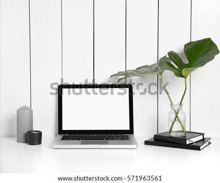 Styled hipster workspace with laptop computer, black notebooks, monstera leaves in vase at home or studio. Desktop computer screen isolated. White desk mockup