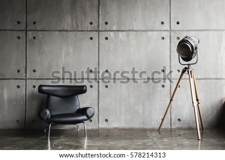 Loft interior mock up photo. Grey block wall with leather black chair and vintage light source lamp. Background photo with copy space for text.