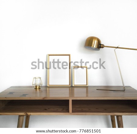 Modern home decor mock-up. Golden frames on wooden design table with gold metal lamp, candle against white wall. Background styled minimal interior mockup.