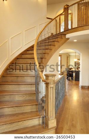 All wood curved staircase with hallway and kitchen in view.
