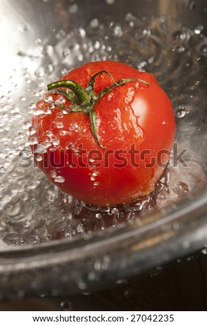 Ripe red tomato splashed with water in stainless steel metal colander.