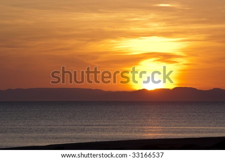 Pink and vibrant red sunset with sun behind mountainous horizon and ocean
