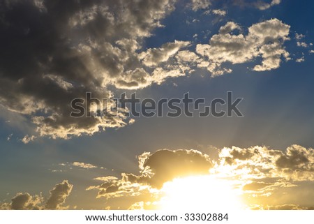 Vibrant sunset with sunbeams across blue sky with scattered white clouds