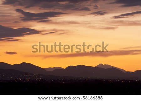 Vivid orange sunset over Colorado foothills. City lights dot hills in lower frame.