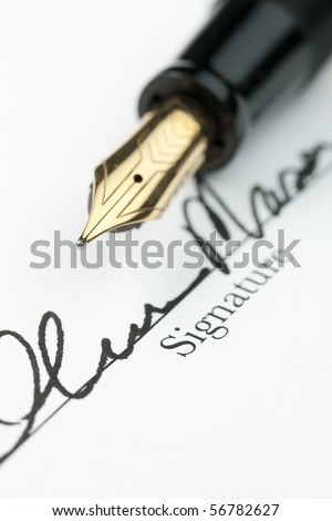 Gold fountain pen over obscured signature on document. Focus on tip of pen nib.