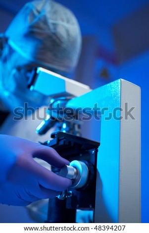Scientist examining sample with microscope in laboratory blue lighting